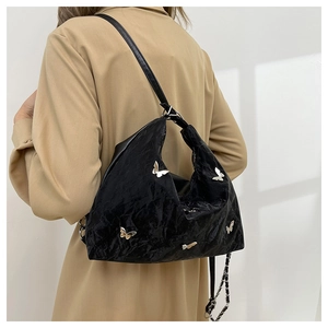 Close-up of a black pleated shoulder bag with silver butterfly charms on a model