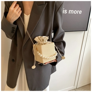 Détail du sac seau tressé crème avec poignée en perles et fine bandoulière dorée