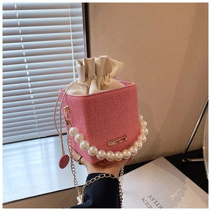 Détail du sac seau rose tressé avec poignée en perles et bandoulière dorée