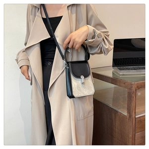 Detail of the black and silver crossbody bag shown on a model wearing a beige trench coat