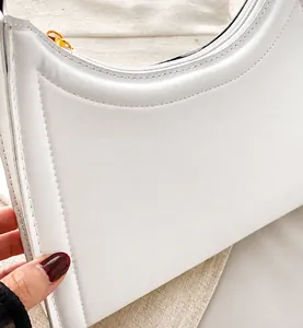 Detail view of white leather crescent bag featuring curved stitching and gold hardware