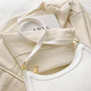 Detail view of the beige baguette bag's adjustable strap and light gold metal buckle