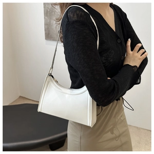 Modern white crescent underarm bag worn by a model in a minimalist art studio setting