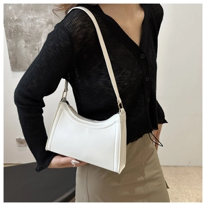 Detailed side view of white baguette shoulder bag worn by model over a black sweater