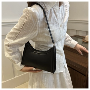 Detail shot of a black leather baguette shoulder bag with gold buckles and chic stitching