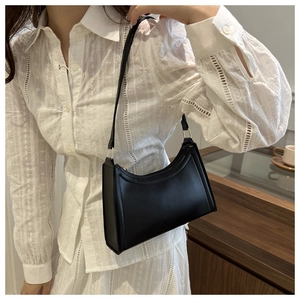 Minimalist black baguette bag shown on shoulder with sleek matte leather finish