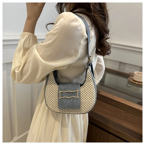 Detail of woven straw saddle bag with blue denim trim and gold buckle worn on shoulder