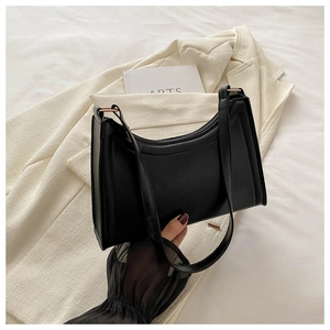Detail of minimalist black baguette shoulder bag with golden metal buckles and fine straps