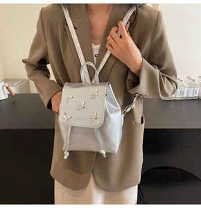 Detail of silver butterfly backpack with metallic finish on a model in a brown blazer