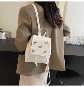 Detail of white mini backpack featuring silver metal butterfly charms and drawstring closure