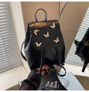 Detailed macro shot of silver butterfly charms on a premium black leather mini backpack