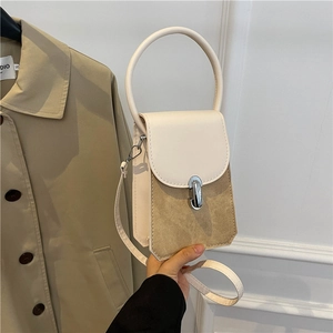 Mini bicolor crossbody bag with round handle and silver metal lock shown with beige trench coat