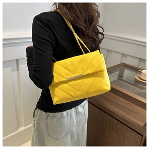 Close-up of bright yellow chevron quilted bag with gold chain strap on a model