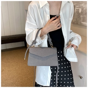 Detail of grey textured flap bag with unique knotted handle and gold metal buckle hardware