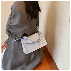 Detail of light grey textured flap crossbody bag with elegant knotted handle design