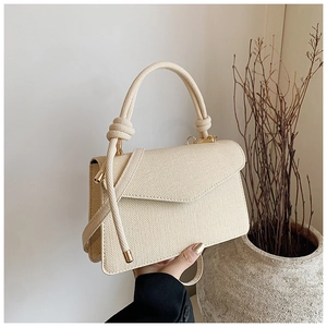 Close-up of cream textured handbag featuring thick rope handles and gold buckle detail