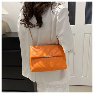 Detail view of orange quilted crossbody bag with gold chain strap worn by a model