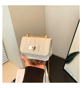 Détail d'un petit sac en paille tressée beige tenu à la main avec chaîne dorée