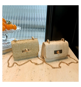 Macro view of woven straw shoulder bag featuring gold chain strap and metal clasp detail