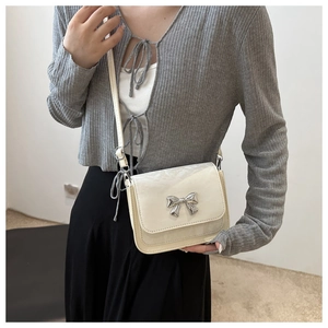 Détail d'un petit sac bandoulière crème avec une boucle papillon en métal argenté