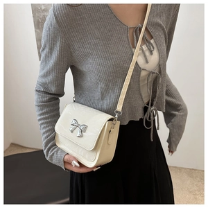 Detail shot of a cream beige crossbody bag with a silver metallic bow decoration