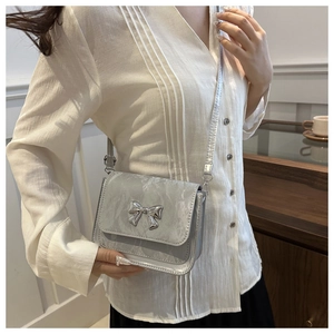Detail of silver metallic crossbody bag featuring a 3D bow buckle and slim shoulder strap