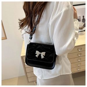 Détail du sac bandoulière en velours noir avec nœud argenté porté par le mannequin