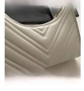 Gros plan du sac baguette en cuir blanc avec texture matelassée en V et fermeture éclair dorée