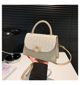 Detail van de beige crossbodytas van stro en leer, vastgehouden door een model in een kamer