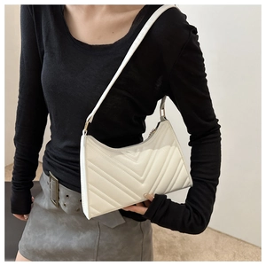 Détail du sac baguette blanc matelassé avec surpiqûres en V sur l'épaule du mannequin