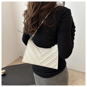 Détail du sac baguette blanc matelassé porté sur une manche longue noire contrastée