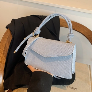Blue and white striped handbag with knot handle detail held against a wooden chair