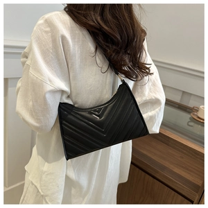 Détail du sac baguette noir matelassé en V sur un mannequin en lin blanc