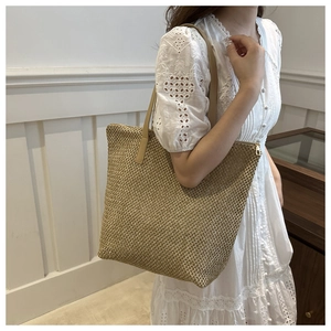 Dettaglio borsa tote in paglia intrecciata a mano con spalline in pelle su una modella