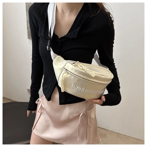 Vue détaillée du sac de poitrine en satin crème avec broderie de lettres et texture soyeuse
