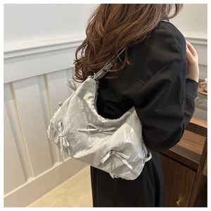 Silver metallic hobo bag with pleated texture and decorative bows worn on the shoulder