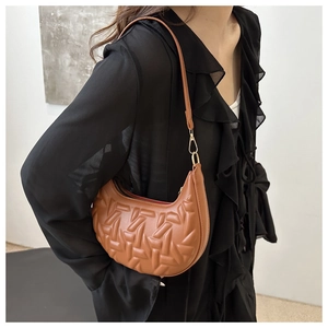 Close-up of brown crescent underarm bag with 3D embossed geometric texture and gold buckle