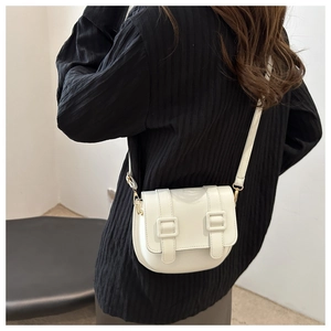 White saddle crossbody bag with leather straps on a black textured garment for contrast