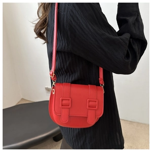 Detailed view of a bright red leather saddle bag with golden hardware on a black top