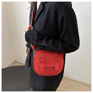Model wearing a small red saddle crossbody bag with parallel buckles on black textured shirt