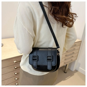 Detail of a black matte leather saddle bag with double buckles on a shoulder-slung model