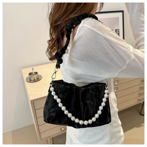 Detail view of black pleated underarm bag with white pearl chain strap on model shoulder