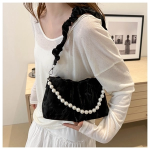 Detail of black pleated velvet handbag featuring a glossy finish and white pearl chain strap