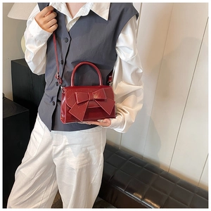 Model wearing a red patent leather mini crossbody bag featuring a large decorative bow