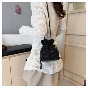 Detail of a black rhinestone drawstring bucket bag worn over the shoulder by a model