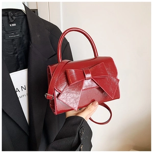 Detail of dark red patent leather crossbody bag with a large decorative bow and top handle