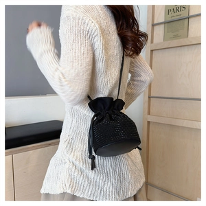Detail of a black woven drawstring bucket bag worn by a model on the shoulder