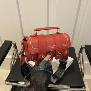 Red cylindrical leather handbag with gold studs and vintage patterned shoulder strap