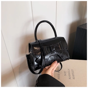 Detail of black glossy bow handbag featuring a shiny patent leather finish and handle