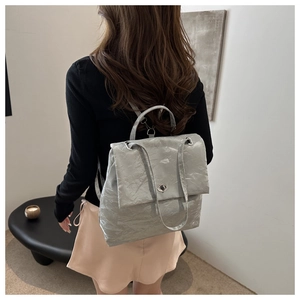 Silver wrinkled fabric backpack detail showing the metallic swivel lock and top handle